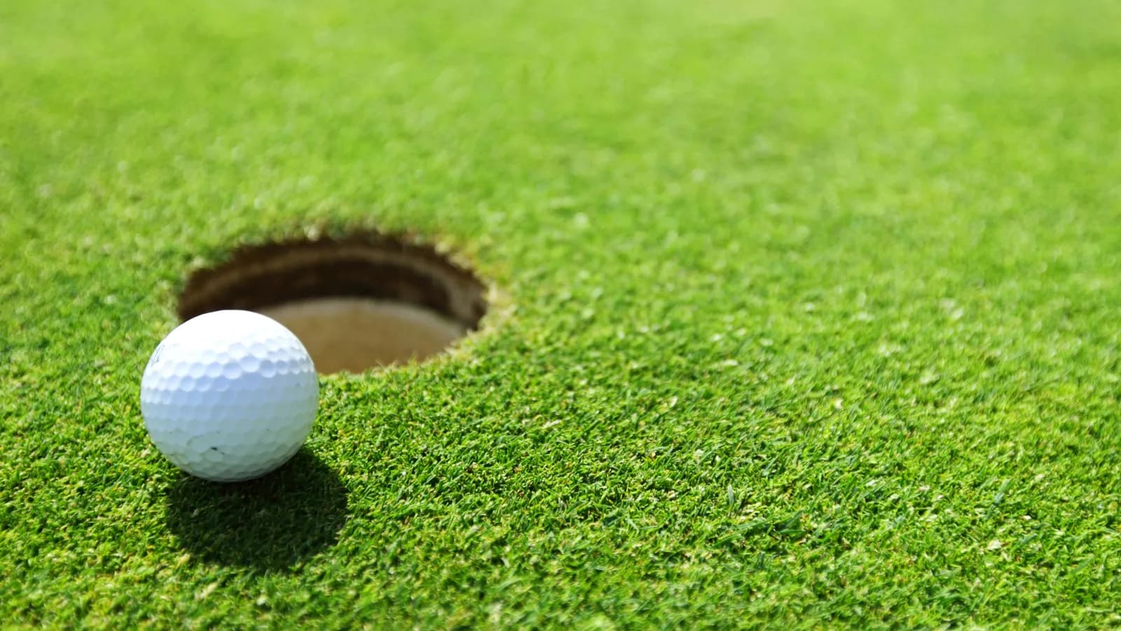 A white golf ball resting on a putting green beside the edge of the hole.